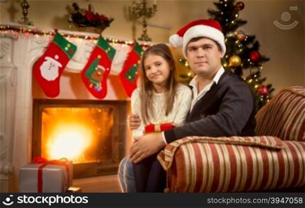 Portrait of happy father and daughter sitting on chair at fireplace
