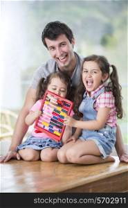 Portrait of happy father and daughters playing with abacus in house