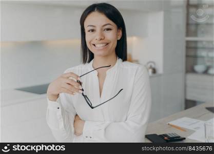 Portrait of happy female business owner standing in modern office. Smiling middle age professional businesswoman leader holding glasses looking at camera on workplace background.. Smiling female business owner in modern office. Portrait of happy businesswoman holding eyeglasses