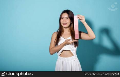 Portrait of happy female hold color card under sun protection, skin beauty face, Asian beautiful young woman smiling and holding skin color scale paper studio shot isolated on blue background