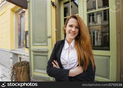 Portrait of happy female owner standing arms crossed outside restaurant