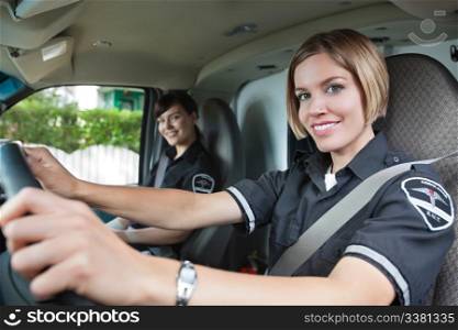 Portrait of happy female paramedic driving ambulance with team member in background