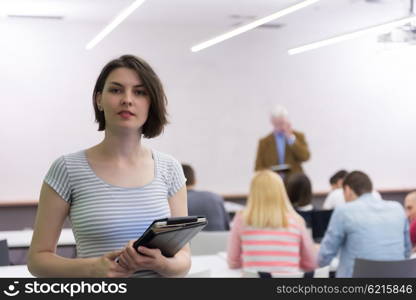 portrait of happy female student holding tablet while teacher teaching students in school classroom