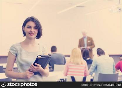 portrait of happy female student holding tablet while teacher teaching students in school classroom