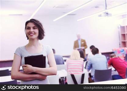 portrait of happy female student holding tablet while teacher teaching students in school classroom
