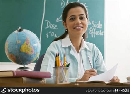 Portrait of happy female teacher at desk