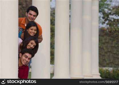 Portrait of happy friends peeking from behind column outdoors