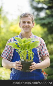 Portrait of happy gardener holding potted plant at nursery