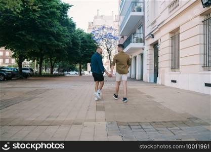 Portrait of happy gay couple spending time together and holding hands in the street. Lgbt and love concept.