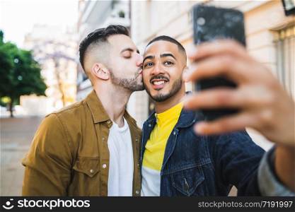 Portrait of happy gay couple spending time together and taking a selfie with mobile phone in the street. Lgbt and love concept.
