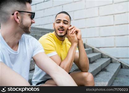 Portrait of happy gay couple spending time together while sitting on stairs outdoors. Lgbt and love concept.