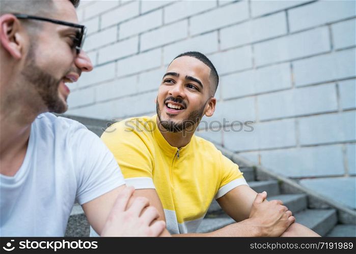 Portrait of happy gay couple spending time together while sitting on stairs outdoors. Lgbt and love concept.