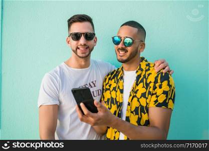 Portrait of happy gay couple spending time together while using mobile phone. Lgbt and love concept.
