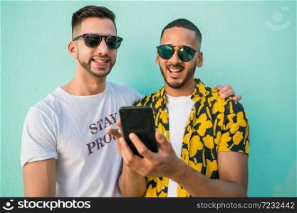 Portrait of happy gay couple spending time together while using mobile phone. Lgbt and love concept.