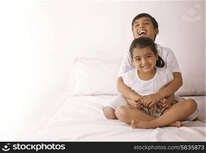 Portrait of happy girl being embraced by brother in bed