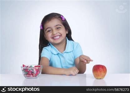 Portrait of happy girl choosing between apple and sweet food against blue background