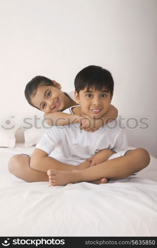 Portrait of happy girl embracing brother from behind in bed