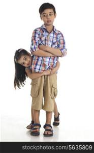 Portrait of happy girl embracing brother from behind over white background