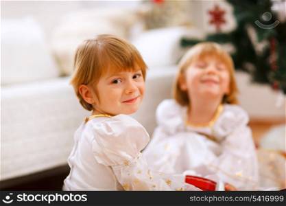 Portrait of happy girl playing with sister near Christmas tree&#xA;