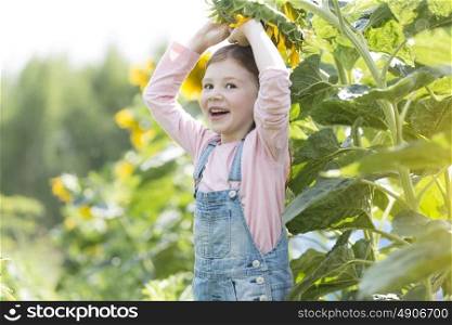 Portrait of happy girl playing with sunflower at farm