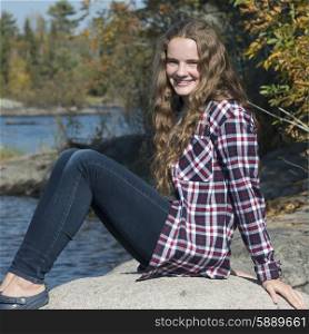 Portrait of happy girl sitting on rock at lakeside, Lake of the Woods, Ontario, Canada