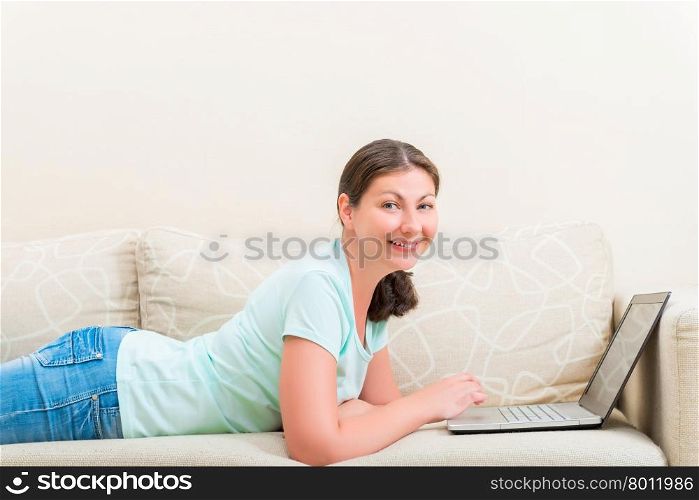 portrait of happy girl with a laptop lying on the sofa