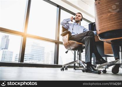 Portrait of happy handsome business man with headset in modern office with city urban building background. Businessman sitting on chair. Caucasian man relaxing in customer care service call center