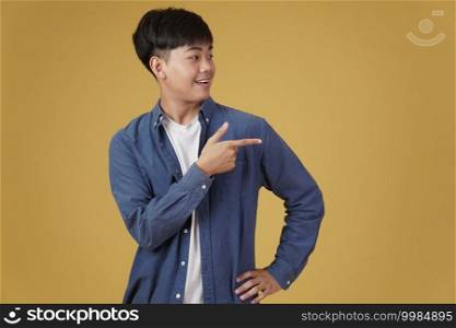 portrait of happy handsome young asian man dressed casually pointing fingers at copyspace isolated on yellow studio background