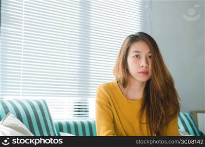 Portrait of happy home owner asian woman with perfect teeth smiling sitting on sofa in the living room in house interior. Relaxing asian woman sitting comfortable in sofa lounge chair smiling happy.