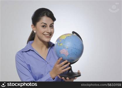 Portrait of happy Indian businesswoman holding globe against gray background