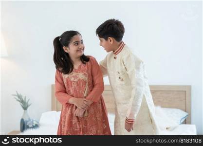 Portrait of happy Indian family handsome teenage brother and little sister embracing standing and talking at bedroom at home, siblings wearing traditional clothing. Family love bonding concept