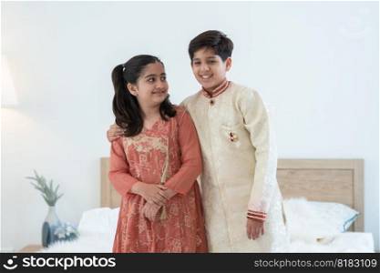 Portrait of happy Indian family handsome teenage brother and little sister embracing standing and talking at bedroom at home, siblings wearing traditional clothing. Family love bonding concept