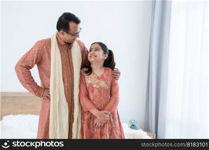 Portrait of happy Indian family, little daughter and middle aged father embracing standing and smiling at each other at bedroom at home, wearing traditional clothing. Family love bonding concept