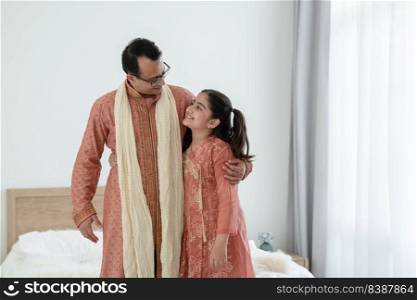 Portrait of happy Indian family standing and hugging in bedroom at home. Smart young father with little cute daughter  wear traditional dress, smiling and embracing each other, warm and cozy mood