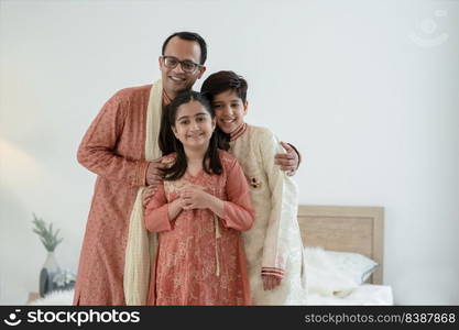 Portrait of happy Indian family standing in bedroom at home. Smart young father with little cute kids wearing traditional dress, smiling and embracing each other with warm and cozy mood