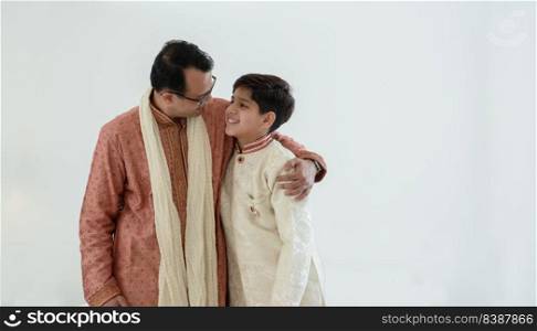Portrait of happy Indian family standing over white background. Smart young father with little handsome son wear traditional dress, embracing each other, smiling, warm and cozy mood. Copy space