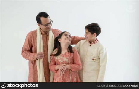 Portrait of happy Indian family standing over white background. Smart young father with little cute kids wearing traditional dress, smiling, looking and embracing each other with warm and cozy mood