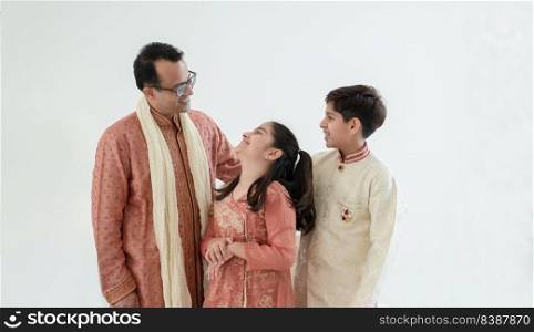 Portrait of happy Indian family standing over white background. Smart young father with little cute kids wearing traditional dress, smiling and looking each other, warm and cozy mood. Copy space