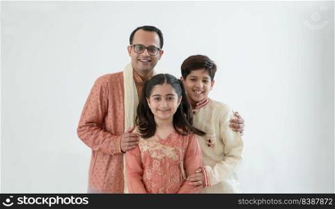 Portrait of happy Indian family standing over white background. Smart young father with little cute kids wear traditional dress, embracing each other, smiling at camera, warm and cozy mood. Copy space