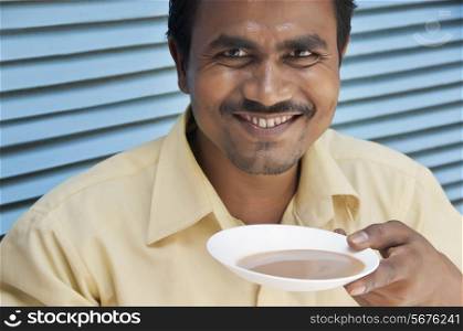 Portrait of happy Indian mid adult man smiling while having chai in saucer