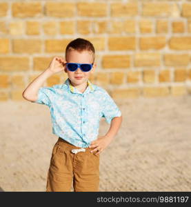 Portrait of happy joyful beautiful little boy wearing blue mirror sunglasses against the yellow brick wall outdoors