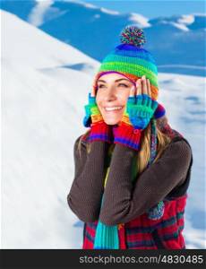Portrait of happy joyful woman having fun outdoors in the snowy mountains, wearing cute colorful hat, scarf and gloves, with pleasure spending winter holidays