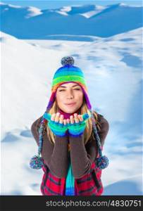 Portrait of happy joyful woman playing outdoors in the snowy mountains sending air kiss, with pleasure spending winter holidays