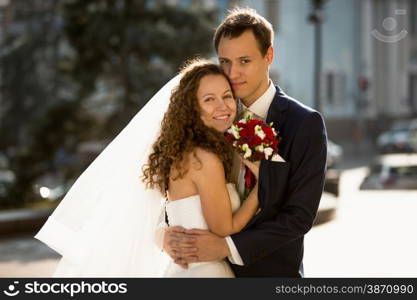Portrait of happy just married couple hugging on street