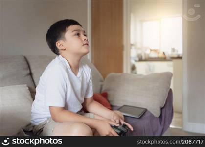 Portrait of happy kid holding a video game control. Child playing a online game at home,Young boy siting on a sofa having fun playing with a toy and relaxing on the weekend, New lifestyle after covid