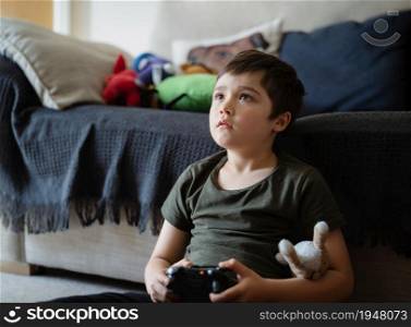 Portrait of happy kid holding video game or game console. Child playing game online at home, Young boy siting carpet having fun and relaxing on his own on weekend, New normal lifestyle concept