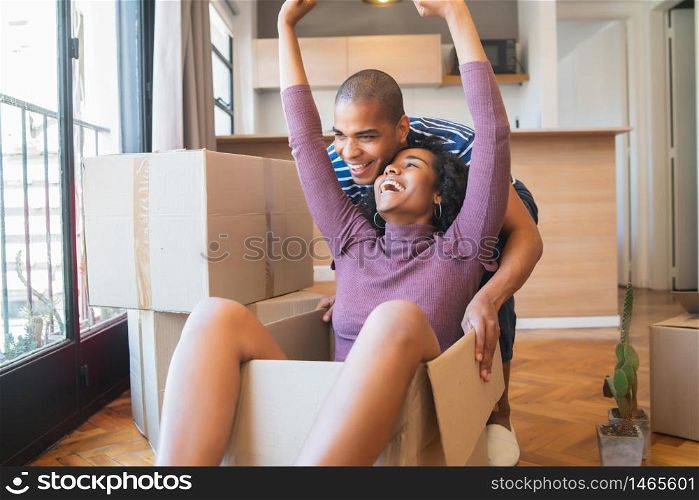 Portrait of happy latin couple having fun with cardboard boxes in new house at moving day. Real estate concept.