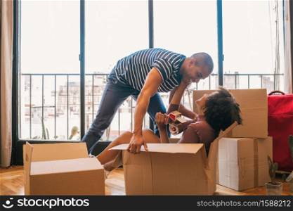 Portrait of happy latin couple having fun with cardboard boxes in new house at moving day. Real estate concept.