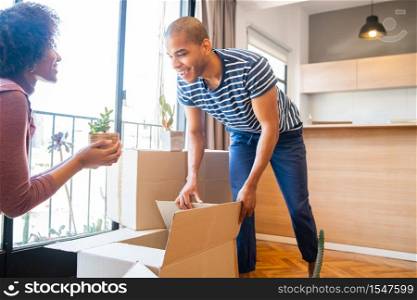 Portrait of happy latin couple packing cardboard box to move in new apartment. Real estate concept.