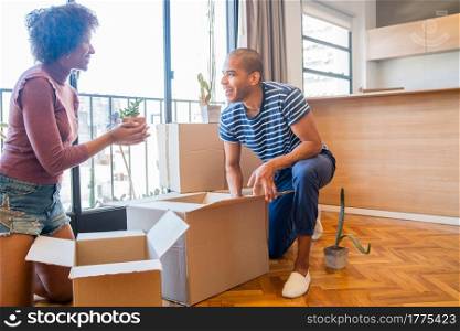 Portrait of happy latin couple packing cardboard box to move in new apartment. Real estate concept.
